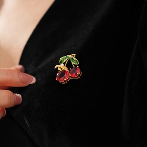 Detail of cherry brooch with red gemstones, green enamel leaves, and pearl bee on black velvet