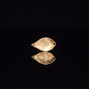Macro shot of gold leaf pendant with fine vein texture on a reflective black background