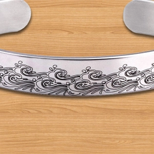 Macro shot of wave relief engraving on silver stainless steel open cuff bracelet
