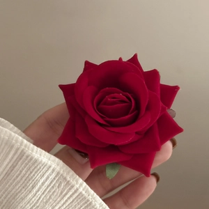 Detail of dark red velvet rose hair clip with green leaf held in hand for close-up view