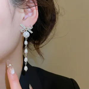 Elegant bow knot stud earrings with long pearl tassels shown on a model side profile