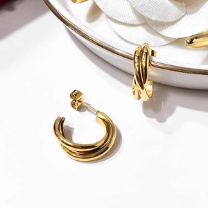 Macro shot of gold multi-layered intertwining hoop earrings on white ceramic tray