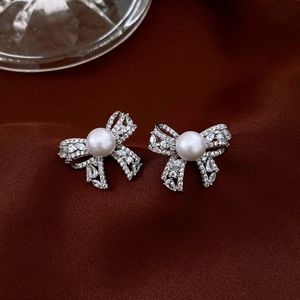 Macro detail of silver bow pearl earrings with cubic zirconia on red velvet