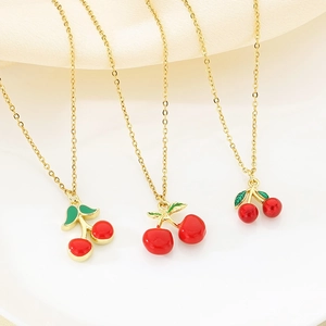 Three gold chain necklaces with glossy red cherry pendants on soft white fabric