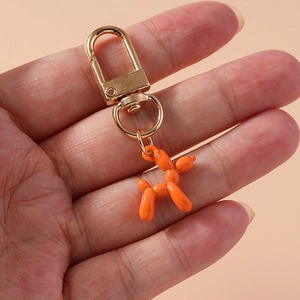 Close-up of bright orange balloon dog keychain with golden lobster clasp on a hand