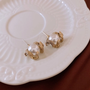 Macro shot of retro pearl earrings with golden vine frames on a ceramic plate