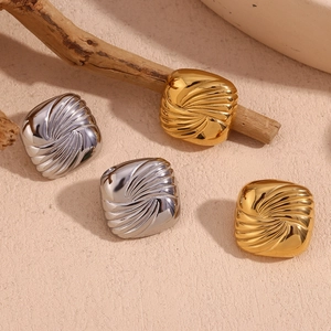 Square textured earrings in gold and silver finish with spiral pattern on beige surface