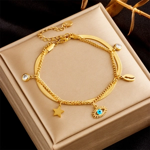 Detailed view of gold double-layer bracelet with evil eye and star charms on matte stand