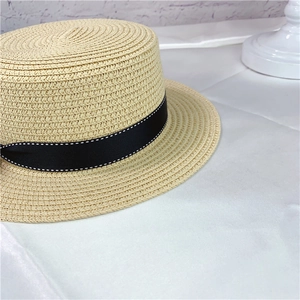 Detail of classic boater hat featuring fine straw weave and black ribbon with stitching