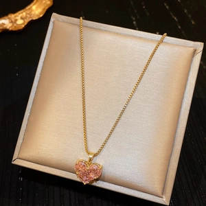 Detailed shot of a gold chain necklace with a pink heart crystal in a beige satin box