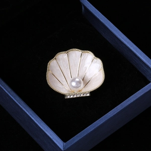 Close-up of white enamel shell brooch with pearl and crystal detail in a jewelry box