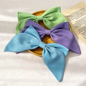 Three large matte fabric bow hair clips in green, purple, and blue on a wooden tray