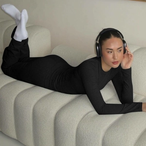 Detail of a black long-sleeve bodysuit shown in a cozy home setting with headphones