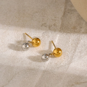 Vue macro de boucles d'oreilles sphériques bicolores or et argent sur pierre beige