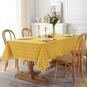 Detail of yellow geometric tablecloth with white fringe tassels on a wooden table