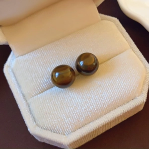 Macro view of round tiger eye stone stud earrings in a beige velvet jewelry box