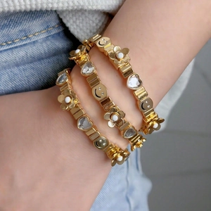 Three-piece gold elastic bracelet set with smiley face, diamond heart, and white flower charms