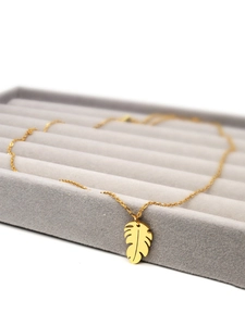 Close-up of gold leaf pendant necklace displayed on a gray jewelry tray