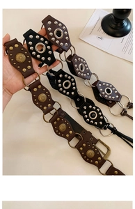 Detail view of retro leather belts with rivets and floral metal pieces on a white desk