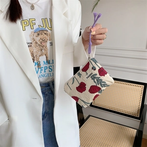 Gros plan d'une pochette florale beige avec motif coquelicot et cordon tressé violet en main