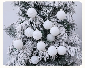 Close-up of white flocked Christmas balls with spiral texture on a snowy pine tree