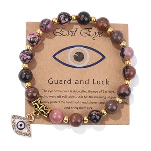 Macro detail of natural stone beaded bracelet featuring a gold evil eye charm pendant