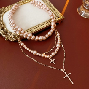 Detail of pink pearl necklace featuring layered gold chains and crystal cross pendants