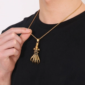 Detail of a gold skeleton hand pendant with skull accents on a twisted rope chain