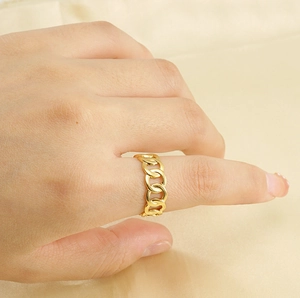 Detailed view of an 18k gold Cuban link chain ring worn on a finger over silk background