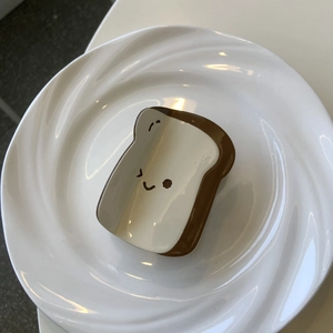 Dettaglio di un fermaglio per capelli a forma di toast con faccina su un piatto bianco