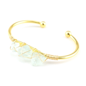 Detail of handmade gold wire-wrapped open cuff featuring three natural green raw stones