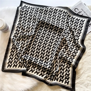 Elegant black and white H-pattern silk scarf displayed on white plush background