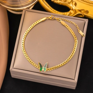 Detail of a gold Cuban chain anklet with a green enamel butterfly charm on a jewelry box