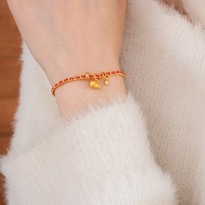 Détail macro du bracelet corde rouge plaqué or avec breloques cœur et gourde au poignet