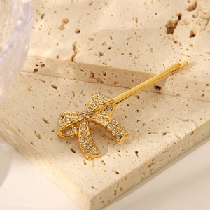 Dettaglio di un fermaglio a fiocco dorato con strass bianchi su pietra beige naturale