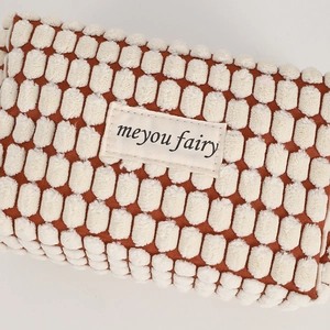 Detailed close-up of reddish-brown textured fabric cosmetic bag with meyou fairy label