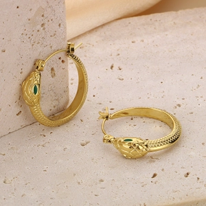 Detail of gold snake hoop earrings with green eye accents and textured scale patterns