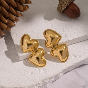 Detailed close-up of gold heart earrings on stone steps with decorative pine cones