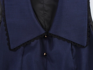 Dettaglio del colletto blu navy con pizzo nero e bottoni in metallo dorato lucido