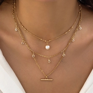 Detail of a three-layer gold necklace featuring white pearls, zircons and a T-bar pendant