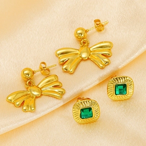 Detail of golden bow earrings and square green gemstone studs on soft fabric