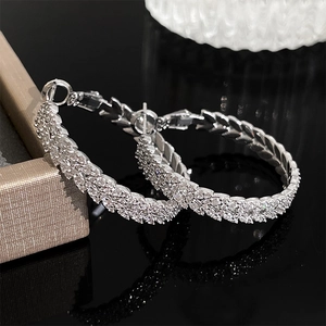 Detailed close-up of silver twist hoop earrings with pavé zircon stones on black surface