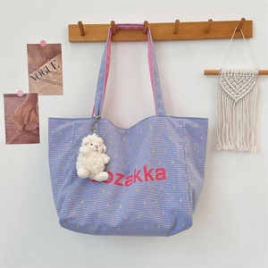 Detail view of a blue checkered tote bag with pink straps and a cute plush lamb pendant