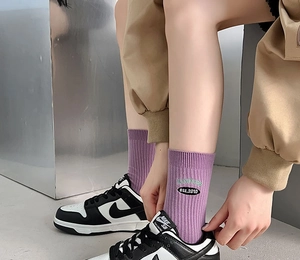 Detail of purple ribbed crew socks featuring XXMPLERS embroidery and white Nike SB sneakers