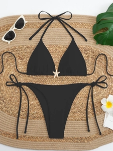 Flat lay of black halter bikini with starfish detail on round straw mat with summer props