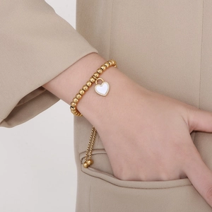 Vue détaillée du bracelet à perles dorées avec breloque cœur blanc au poignet