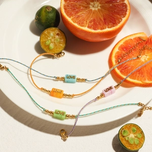 Colorful woven cord bracelets with engraved LOVE charms on a white ceramic plate