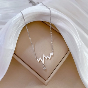 Detail view of a silver heartbeat wave pendant with a small zircon on white silk background