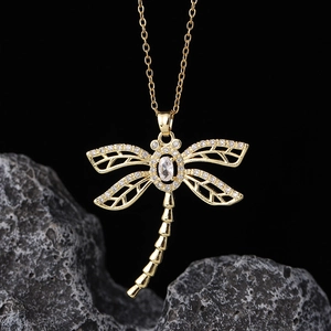 Macro detail of gold dragonfly pendant with pave-set crystals on rough stone background