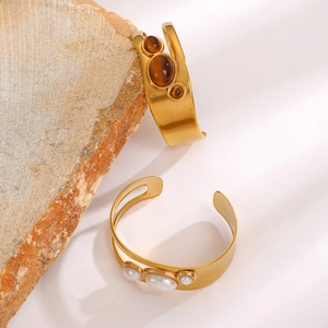Detail of gold hollow cuff bracelets with tiger eye stones and white round pearls
